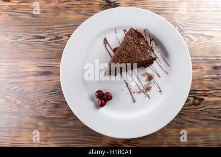 Torta al cioccolato sulla piastra bianca su sfondo di legno. Foto Stock