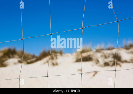 Sottile filo ritorto recinzione aginst impostato un profondo cielo blu adn scrubby duna di sabbia sulla costa spagnola Foto Stock