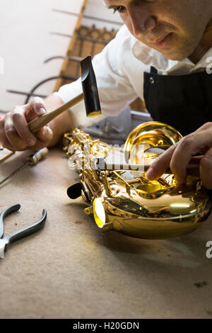 Strumento maker con un martello la riparazione di un sassofono Foto Stock