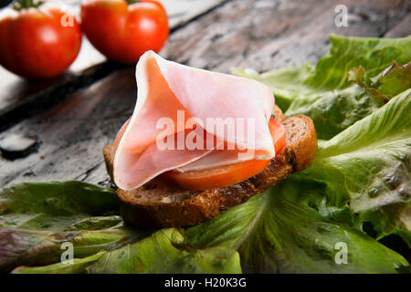 Bruschetta con prosciutto di maiale e pomodoro su una fetta di pane sulla tavola di legno Foto Stock