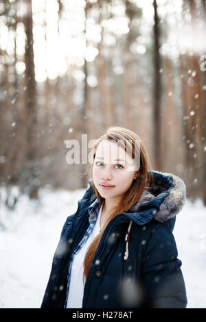 Giovane donna in abiti invernali in piedi sotto la neve, guardando la fotocamera. In inverno il paesaggio della foresta e la caduta di neve sullo sfondo Foto Stock