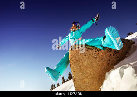 Snowboarder ragazza siede sulla pietra blu sullo sfondo del cielo Foto Stock