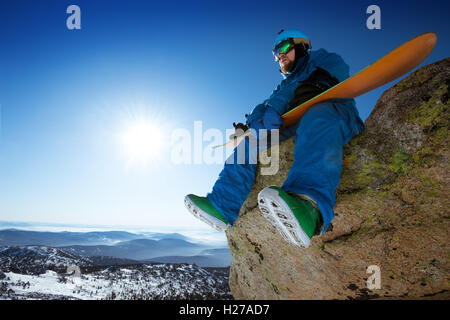 Snowboarder si siede sul cielo blu sullo sfondo di montagne Foto Stock