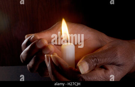 La mano dell'Africano che tiene una candela illuminata, simboleggia il calore, la sicurezza e la luce. Foto Stock