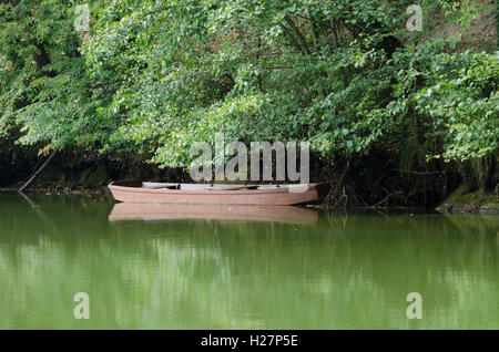 La barca di legno e fogliame riflessa nel lago calmo Foto Stock