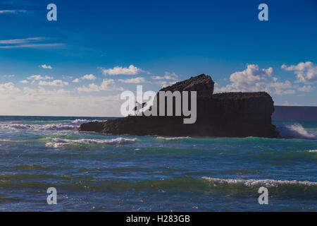 L uomo non identificato con la tavola da surf sulla grande roccia di montagna a Tonel Beach, Sagres Portogallo Foto Stock