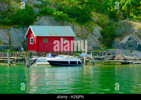 Askeron, Svezia - 9 Settembre 2016: ambientale documentario di red boathouse sull isola con barche da diporto in primo piano. Gree Foto Stock