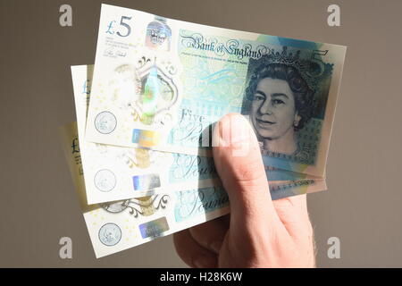 Close up di un ragazzo adolescente tenendo tre nuovo polimero cinque pound note Foto Stock