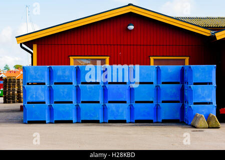 Mollosund, Svezia - 9 Settembre 2016: ambientale documentario di blu cassette in plastica impilati al di fuori di un rosso e giallo sede, Foto Stock