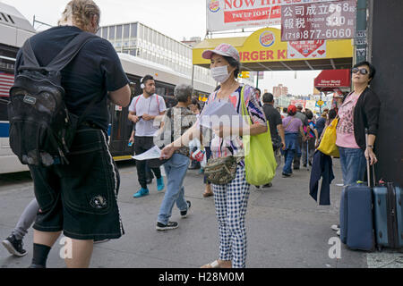 Un americano asiatico donna che indossa una maschera facciale, distribuendo volantini sulla strada principale nel centro di lavaggio, Queens, a New York City Foto Stock