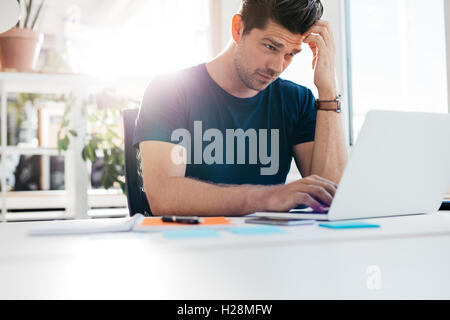 Colpo di giovane uomo utilizzando laptop e guardando preoccupato. Imprenditore lavorando alla sua scrivania. Foto Stock