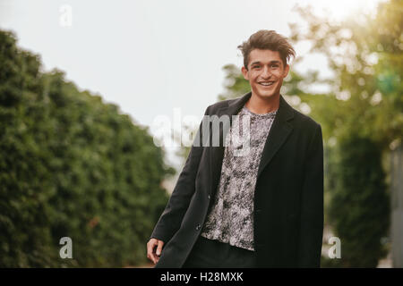 Ritratto di bel giovane uomo in piedi all'esterno guardando la fotocamera e sorridente. Ragazzo adolescente in casuals cercando felice. Foto Stock