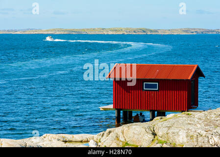 Mollosund, Svezia - 9 Settembre 2016: ambientale documentario di red boathouse su palafitte con il motoscafo facendo un giro in Foto Stock