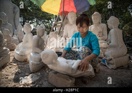 Una donna locale pulisce e lucida il marmo statue di Buddha nella sua officina, Amarapura, Myanmar. Foto Stock