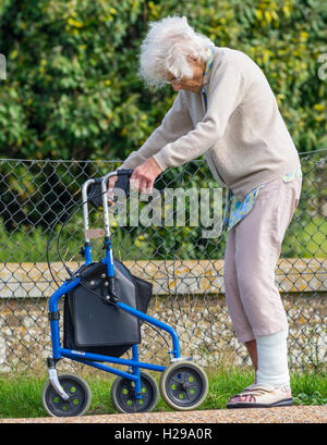 Signora anziana camminare con l'aiuto di un telaio a piedi con ruote, in Inghilterra, Regno Unito. Rollator o a ruote Zimmer frame. Foto Stock