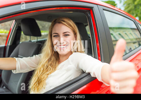 Felice sorridente ragazza in un auto rossa mostra il pollice verso l'alto. Concetto di viaggio. Foto Stock