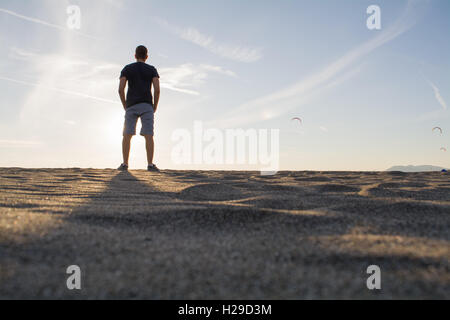 Guy standing sulla sabbia e guardare il kite surfers Foto Stock