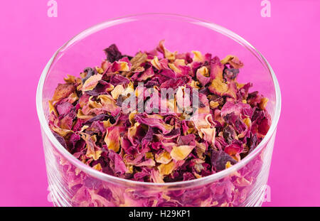 Petali di rosa in una ciotola di vetro su rosa. Fiori Secchi, utilizzato per profumi, cosmetici, tè e bagni. Foto Stock