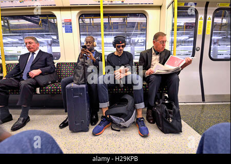 Londra, Inghilterra, Regno Unito. Passeggeri su una Londra metropolitana, treno ascoltando musica / lettura Foto Stock