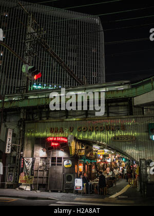 Tokyo dopo il tramonto. Linea Yamamote treno su tracce elevata in precedenza occupato ristoranti con patroni a street tabelle, . Gaado-shita, Yurakucho, Tokyo, Giappone Foto Stock