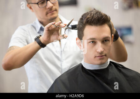 Shot interni del processo di lavoro in moderno barbiere. Close-up ritratto di attraente giovane ottenere taglio di capelli alla moda. Ha maschio Foto Stock