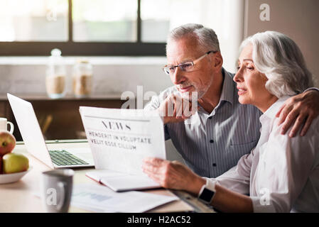 Felice e premurosa vecchia coppia lettura giornale in cucina Foto Stock