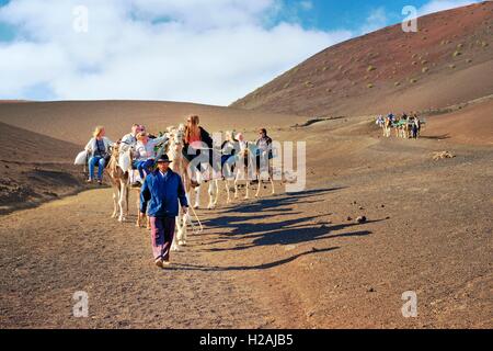 Tourist giri in cammello Echadero de los Camellos attraverso il paesaggio vulcanico. Parco Nazionale di Timanfaya, Lanzarote, Isole Canarie Foto Stock