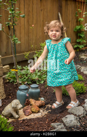 Diciotto mesi di età ragazza camminare fuori in un giardino dove ci sono le urne di ceneri da cani, Issaquah, Washington, Stati Uniti d'America Foto Stock