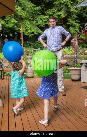 Padre scherzosamente deliberando coraggioso quando i suoi tre e un anno di età le figlie stanno per lanciare palle di lui Foto Stock