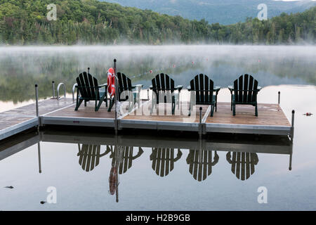 Poltrone Adirondack sul cuore il lago di dock in una nebbiosa mattina in alte vette regione del Adirondacks vicino a Lake Placid, NY Foto Stock