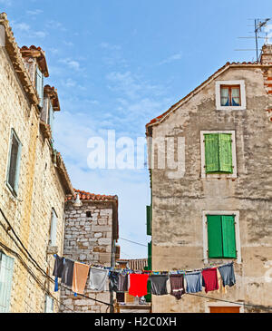 Split, Croazia, vecchie case di città, persiane alle finestre, lavaggio appeso su una linea. Cielo blu Foto Stock