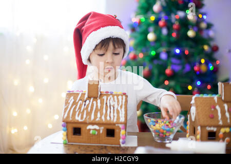 Carino piccolo ragazzo, rendendo gingerbread cookies house, la decorazione a casa nella parte anteriore dell'albero di Natale, bambini che giocano e godendo Foto Stock