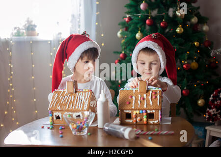 Due ragazzi dolce, fratelli, rendendo gingerbread cookies house, la decorazione a casa nella parte anteriore dell'albero di Natale, bambini che giocano e Foto Stock