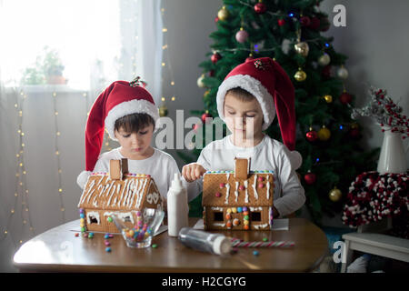 Due ragazzi dolce, fratelli, rendendo gingerbread cookies house, la decorazione a casa nella parte anteriore dell'albero di Natale, bambini che giocano e Foto Stock