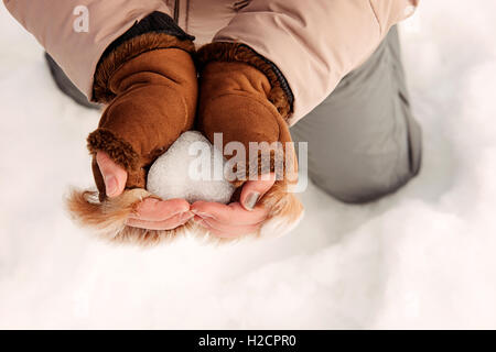 Donna che mantiene a forma di cuore snowball, close-up delle mani Foto Stock