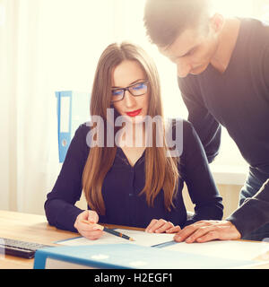 Due impiegati a discutere circa le carte al banco. Il business aziendale persone cercano attraverso documenti aventi la conversazione Foto Stock