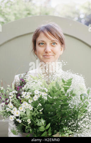 Ritratto di una donna sorridente portando un mazzo di fiori bianchi. Foto Stock
