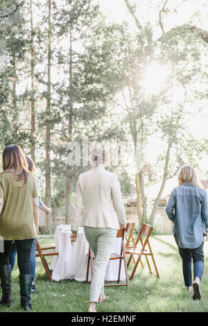 Tre donne in cammino verso un tavolo e sedie in un giardino. Foto Stock