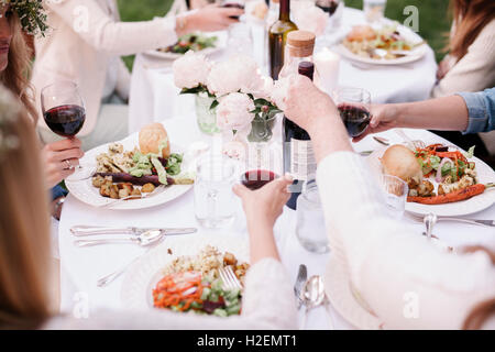 Il gruppo di amici di sesso femminile si sono riuniti intorno ad un tavolo, di tostatura con vino rosso. Foto Stock