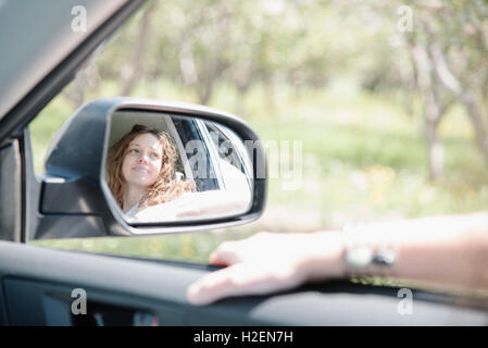 La donna in una vettura in un viaggio su strada, guardando fuori della finestra, la riflessione si vede nel lato specchietto. Foto Stock