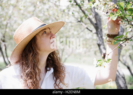 Una donna in un cappello di paglia, sotto un albero di mele in fiore. Foto Stock