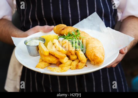 Un pasto cucinato, un piatto di pesce e patatine fritte con guarnire e tartare di salsa. Foto Stock