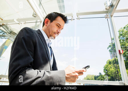 Imprenditore che indossa un abito grigio in piedi all'aperto, utilizzando il suo telefono cellulare. Foto Stock