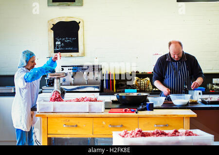 Donna che indossa indumenti di protezione e guanti e uomo che indossa una striata grembiule blu lavorando in una macelleria. Foto Stock