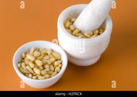 I pinoli in bianco ciotola e mortaio su sfondo arancione. Semi commestibili di pini coreani famiglia Pinaceae, Pinus koraiensis. Foto Stock