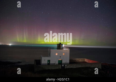 L'Aurora Boreale appaiono nel cielo sopra Bamburgh lighthouse a feste di addio al celibato Rock in Northumberland. Foto Stock