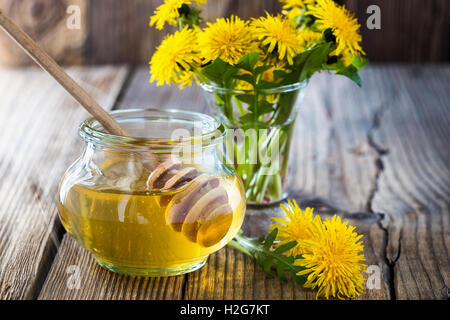 Il miele di fiori in un vaso di vetro e il tarassaco su un tavolo di legno Foto Stock