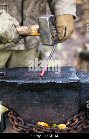 Fabbro forges caldo asta in acciaio con martello sull'incudine in outdoor fucina rurale Foto Stock