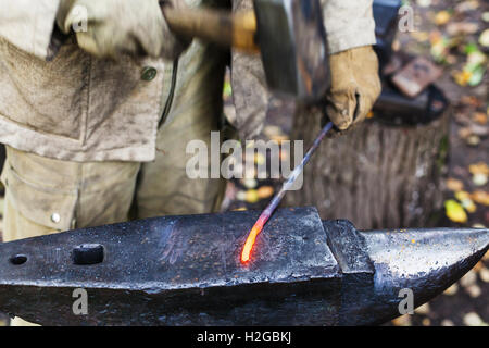 Fabbro martellamento red hot tondino di ferro sull'incudine in outdoor fucina rurale Foto Stock