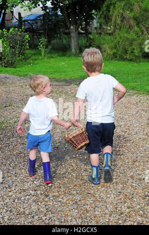 Due piccoli ragazzi di età compresa tra 2 e 5 anni, portando un cesto tra di loro, andando a raccogliere le uova. Foto Stock